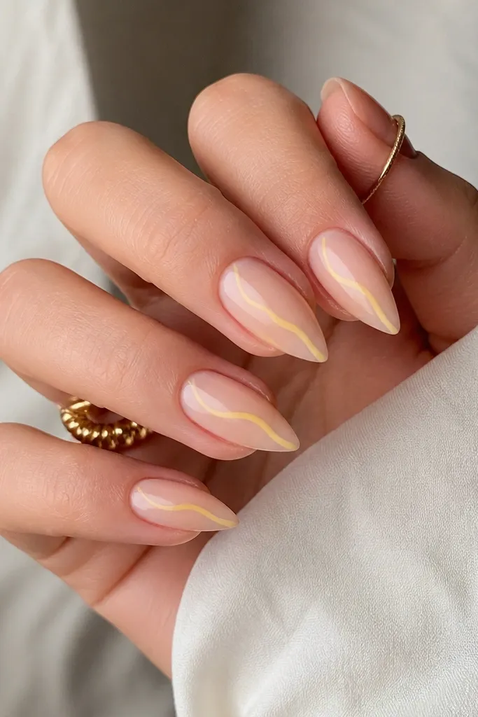 Short stiletto nails with a sheer nude base. A single butter-yellow line draws from the outer side of the nail to the tip point, like a thin lightning bolt line. Glossy finish.