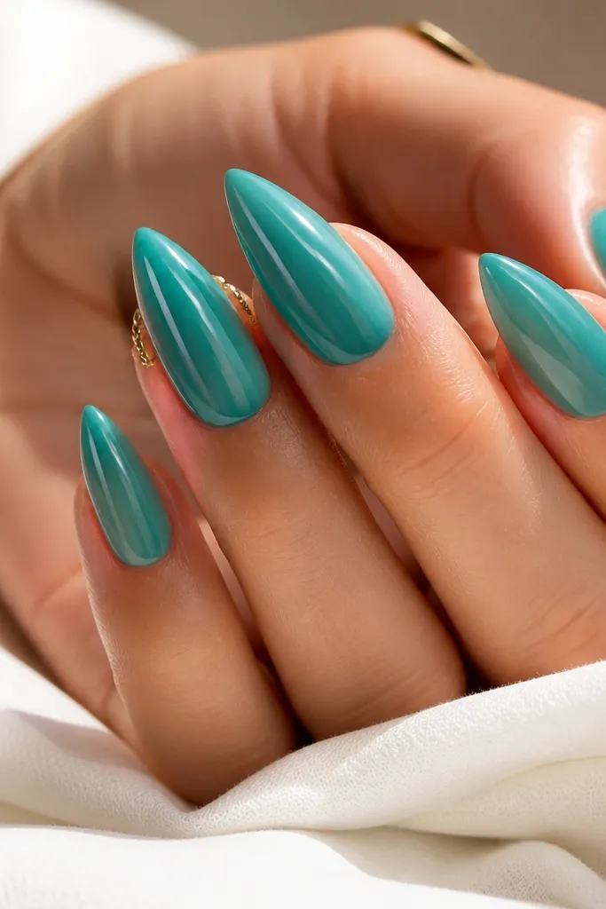 Short stiletto nails painted sea-glass teal. Two thin clear lines run down each side of the nail from mid-nail to the tip point, like glass edges. Glossy.
