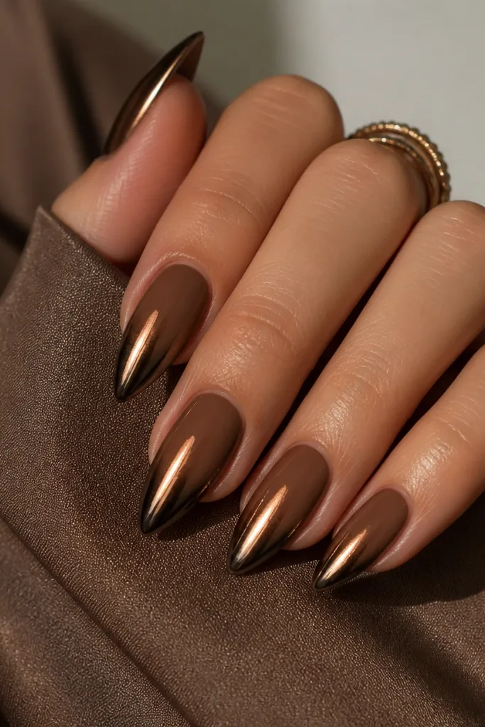 Short stiletto nails with a warm cocoa-brown base. The free edge is coated in a dark bronze chrome that fades slightly into the brown. High shine.
