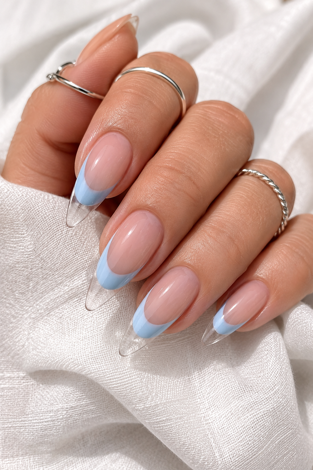 Short stiletto nails with a sheer nude base. A sky-blue French band sits at the free edge, but the very tip point is left clear, creating a sharp white-space triangle. Glossy top coat.