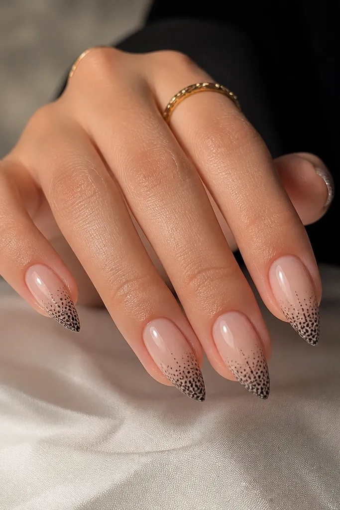Short stiletto nails with a sheer nude base. Near the tip, a lace-like pattern appears as tiny black dots, fading from dense at the free edge to almost invisible toward mid-nail. Glossy.