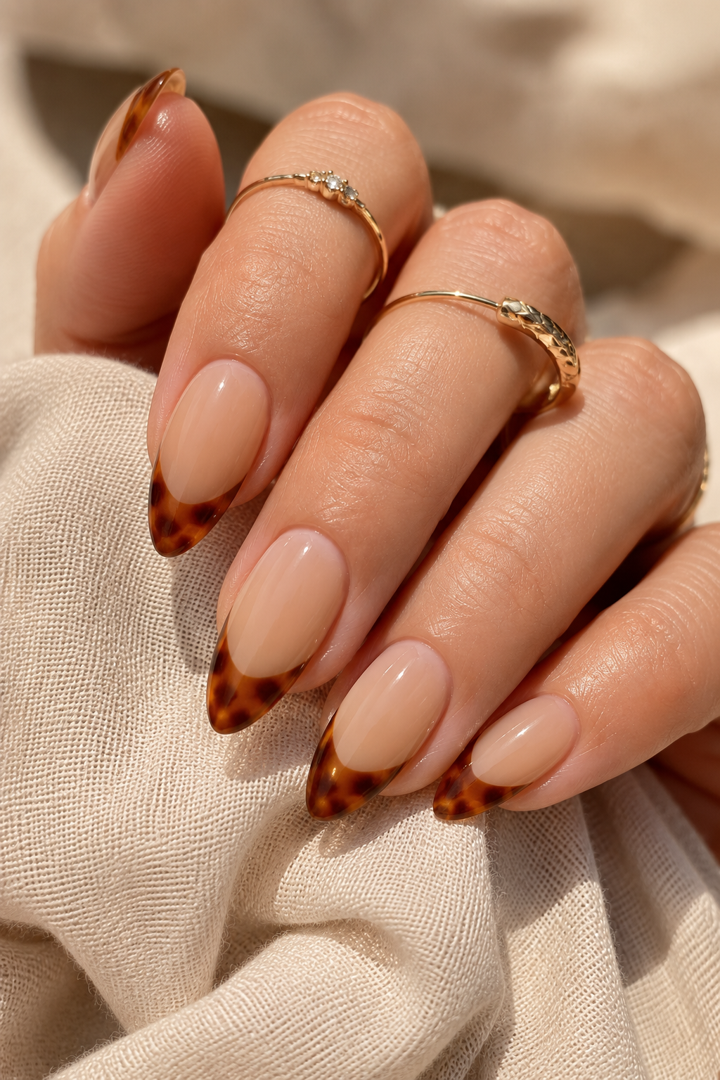 Short stiletto nails in creamy beige. The free edge has tortoise-shell style swirls in caramel and dark brown, concentrated near the tip point. Glossy.