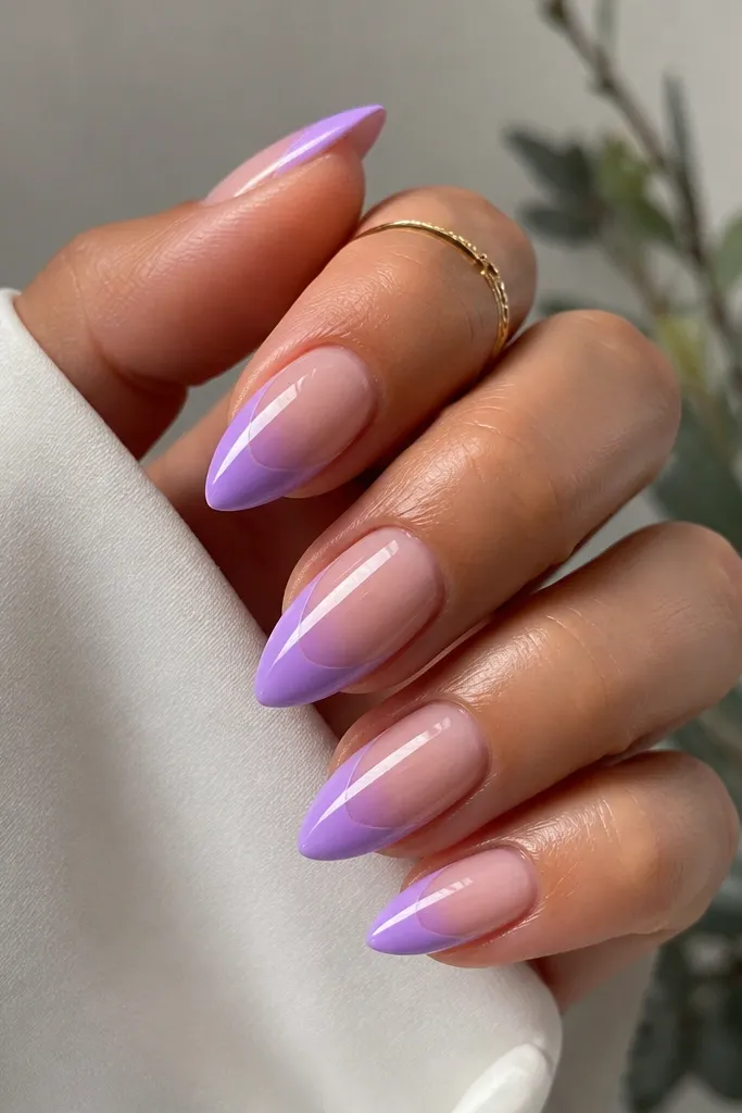 Short stiletto nails with a lavender-to-lilac gradient concentrated at the tip. A thin clear outline traces the outer edge of the stiletto shape from mid-nail to the tip point. Glossy.