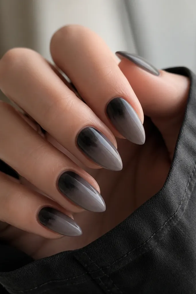 Short stiletto nails with a smoky gray base. Near the cuticle, a soft black cloud shape sits like a shadow, fading outward. Glossy finish.