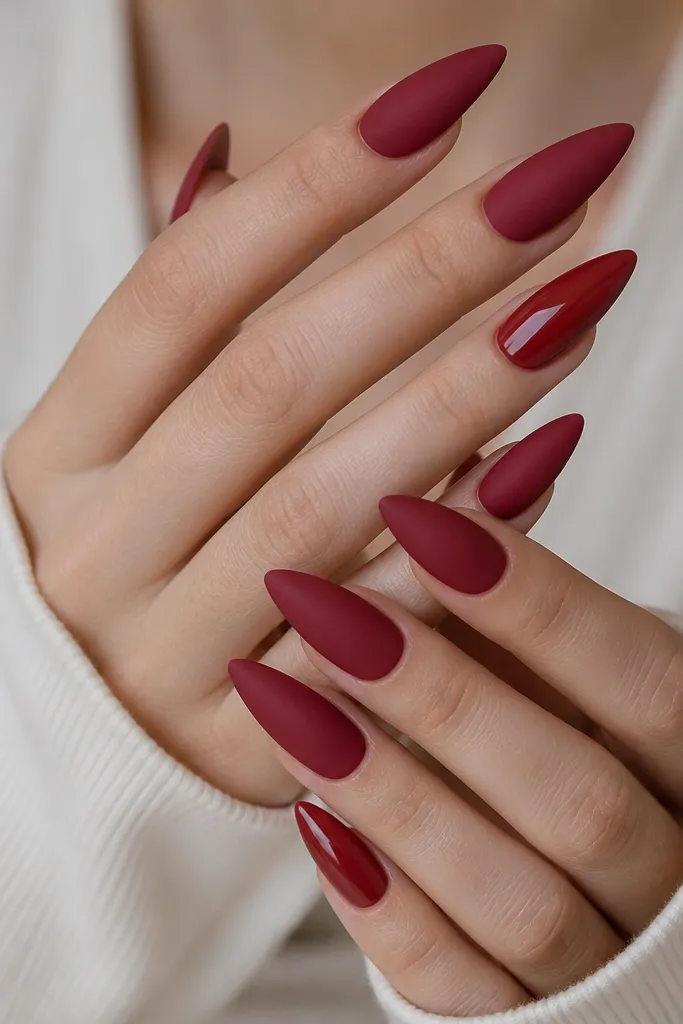 Four nails are matte deep red with a soft, velvety finish. One accent nail on each hand is the same red but glossy and reflective, with a smooth stiletto point.