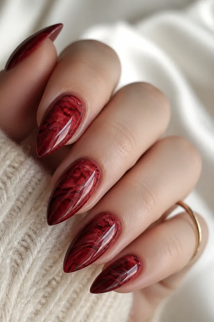 Short stiletto nails with deep red marble swirls. Fine black pinstripes run through the veins like hairline cracks. The finish is glossy and smooth.