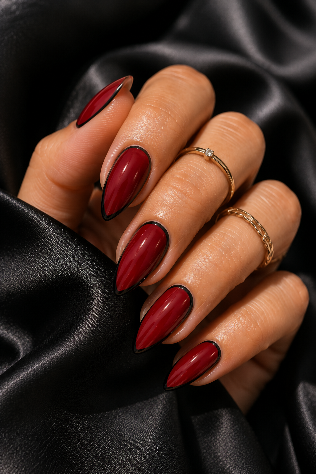 Short stiletto nails painted blood red glossy. A super thin black line outlines the sides of the nail from mid-length to the tip, like a razor edge.
