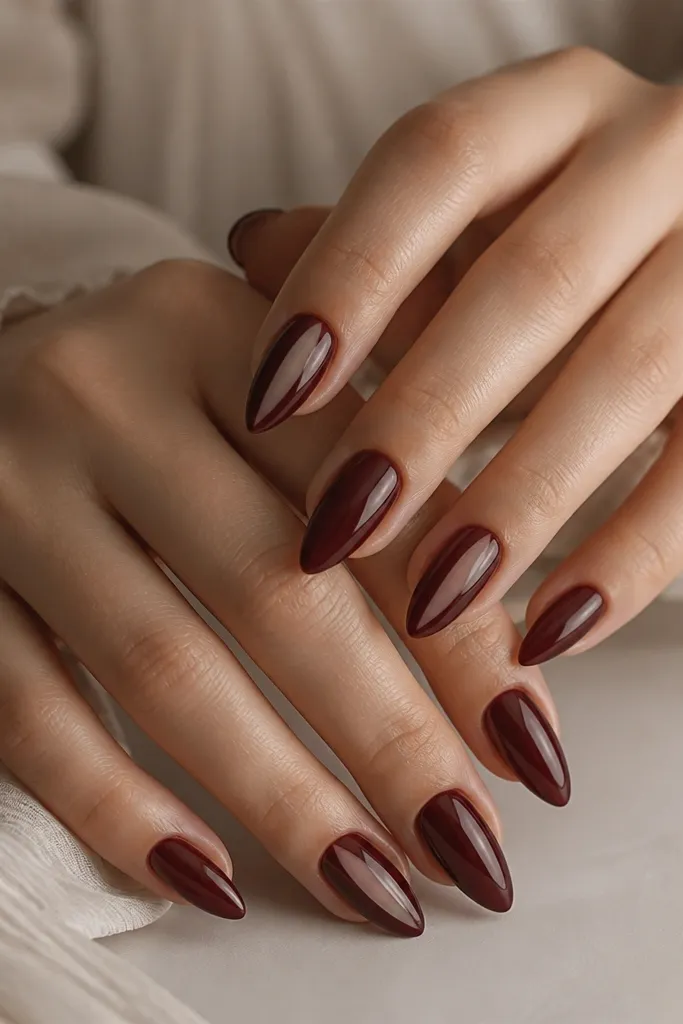 Short stiletto nails painted oxblood red. On one nail per hand there's a small vertical window of bare nail near the center, framed by red. Glossy finish.