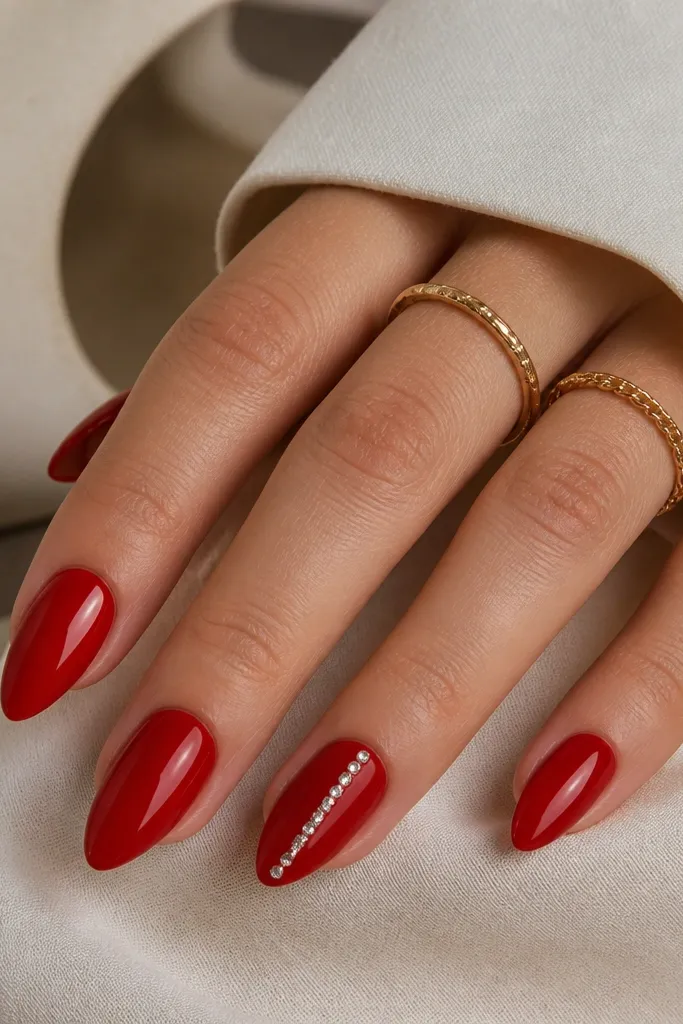 Short stiletto nails in cherry red glossy. One accent nail has a straight line of tiny clear micro rhinestones running from near the cuticle to the mid-length. Other nails are solid red.