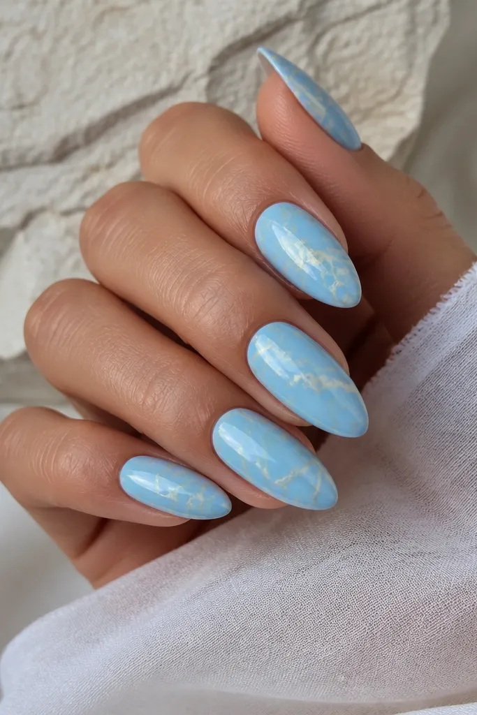 Almond nails with sky blue as the dominant base. Fine soft-yellow veins run through the blue like marble cracks. Finish is glossy with a natural stone look.