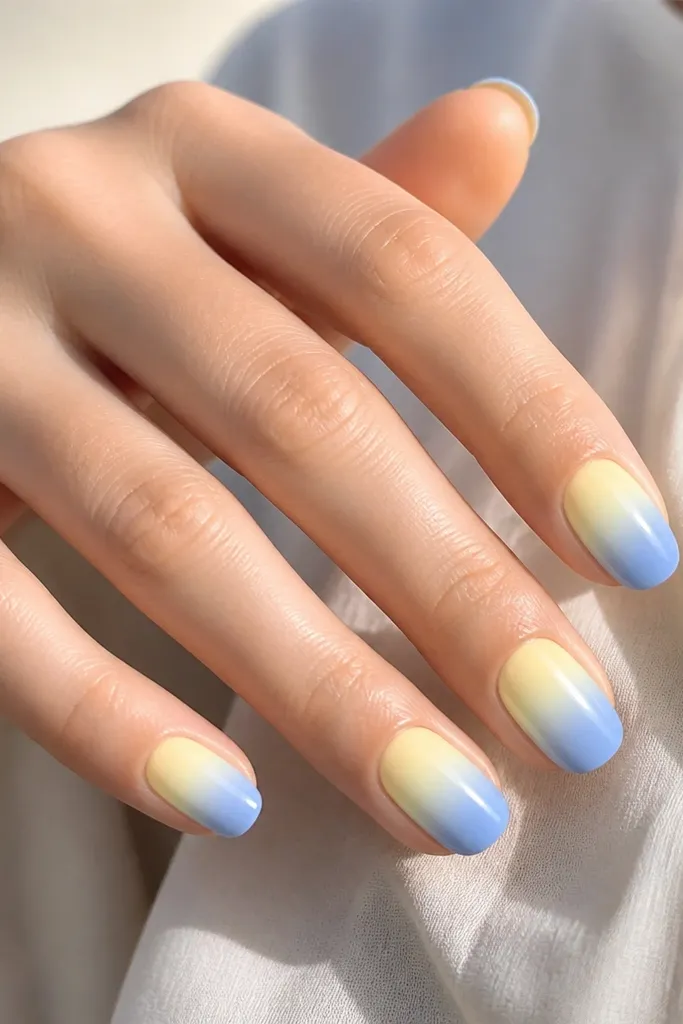 Nails start with a pale lemon-yellow near the cuticle and fade into cornflower blue at the tips. The transition is smooth, with no harsh line. Glossy finish.