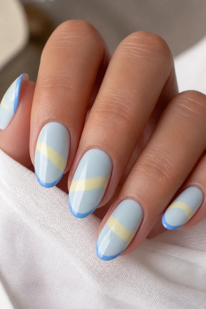 Light blue base nails. On each nail, a soft yellow swoosh runs diagonally across the middle. The tip has a thin blue outline just like a French edge. Glossy finish.