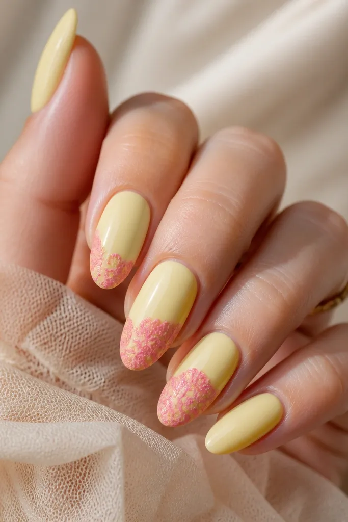 Nails painted in a glossy light yellow. On two accent nails, there is a pink lace-like decal pattern running vertically near the center, with tiny cut-out details.
