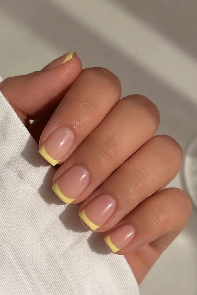 Short square nails with glossy nude base. The French tips are painted light yellow and finished matte, creating a clear contrast. Edges are sharp and even.