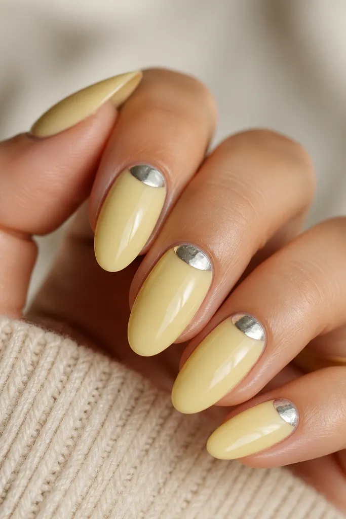 Glossy pale yellow nails with a silver foil half-moon at the cuticle. The foil has irregular edges and catches light.
