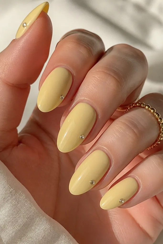 Nails in solid light yellow jelly glossy finish. On each nail, a single tiny rhinestone sits at the outer corner near the tip, like a sparkle point.