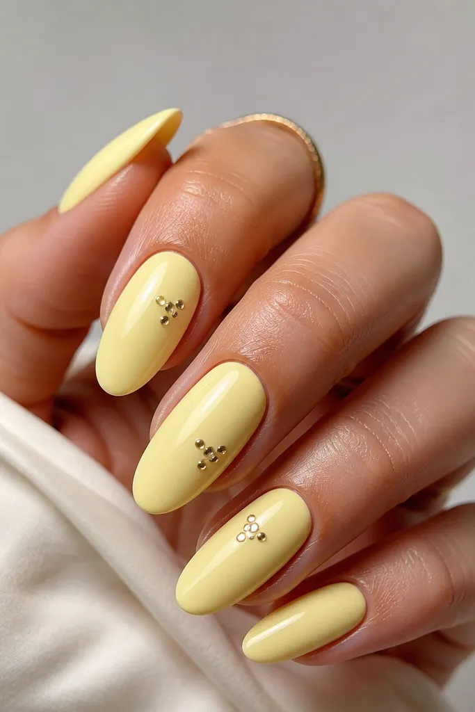 All nails are glossy pale yellow; each nail has tiny silver chrome dot clusters near the cuticle - like 3-4 micro dots in a loose triangle.