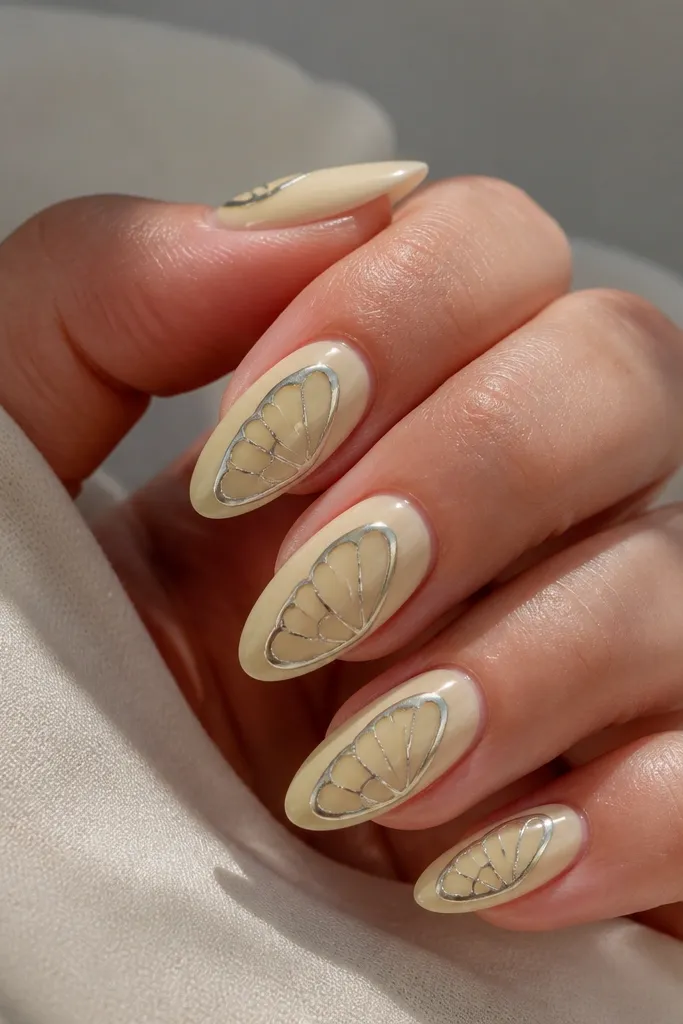 Light yellow nails with a chrome outline drawing butterfly wings across one side of each nail; the outline is silver mirror with negative space inside the wings.