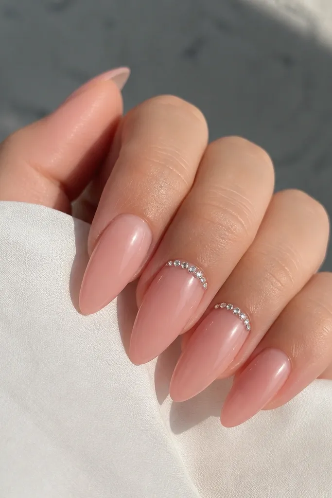 Short stiletto acrylic nails in sheer pink with a glossy finish; tiny clear crystals placed right along the cuticle line on two accent nails.