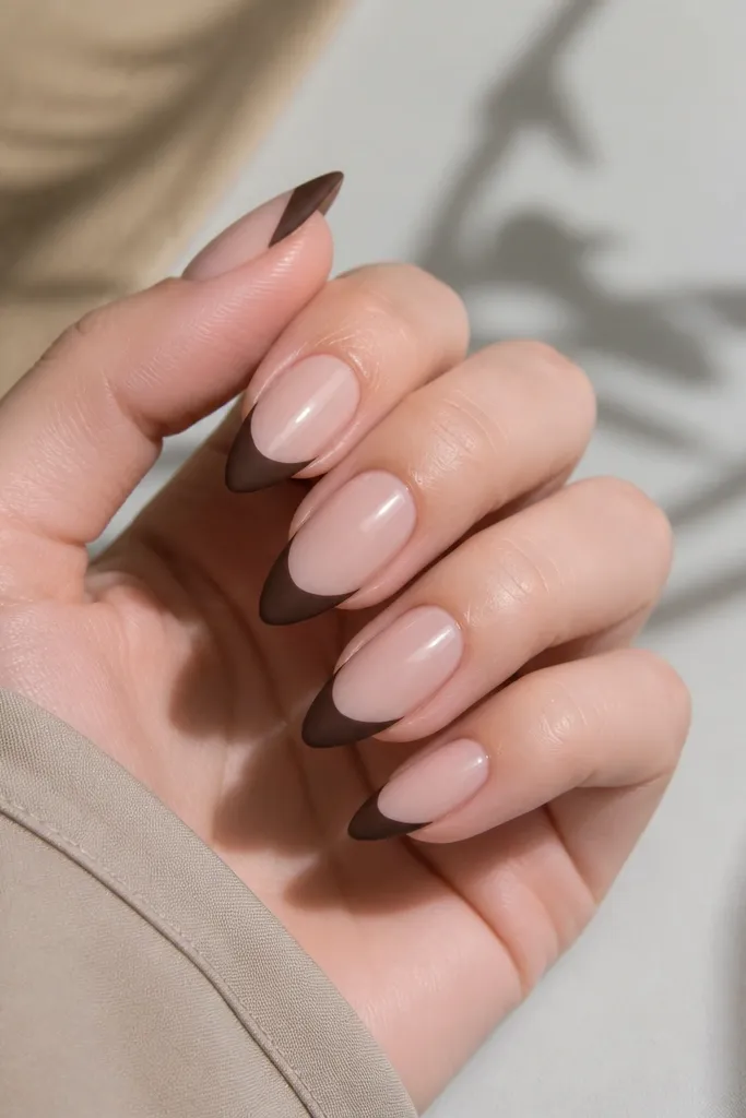 Short stiletto nails with a nude base and deep chocolate brown tips; the tips have a soft, matte-velvet texture while the base looks glossy.