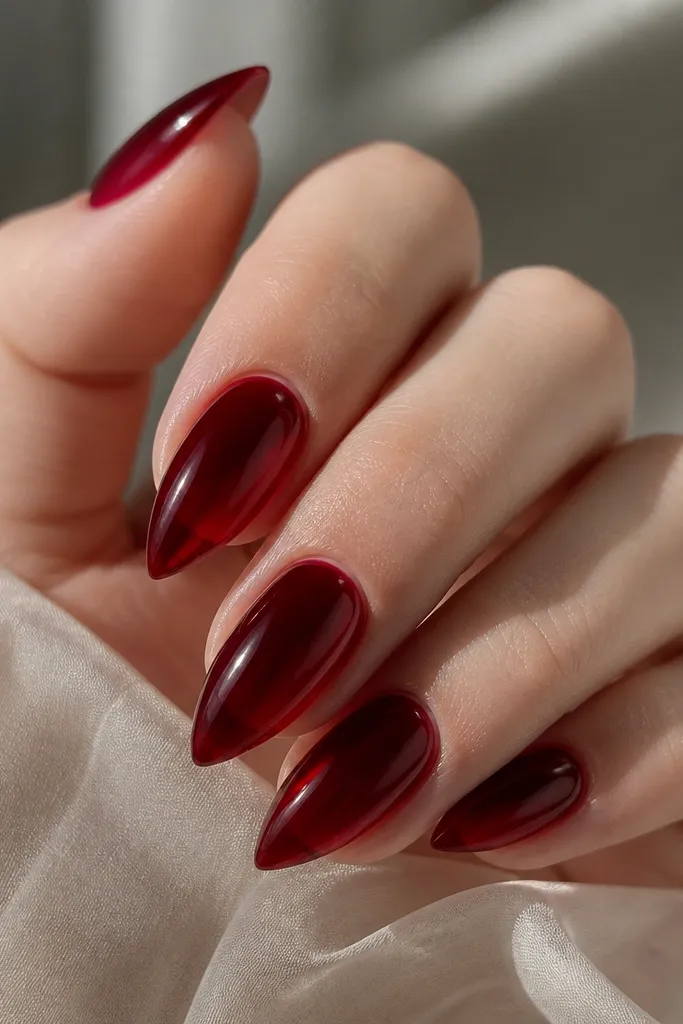 Short stiletto nails with a translucent deep burgundy jelly look, glossy finish, subtle light-catching glow.