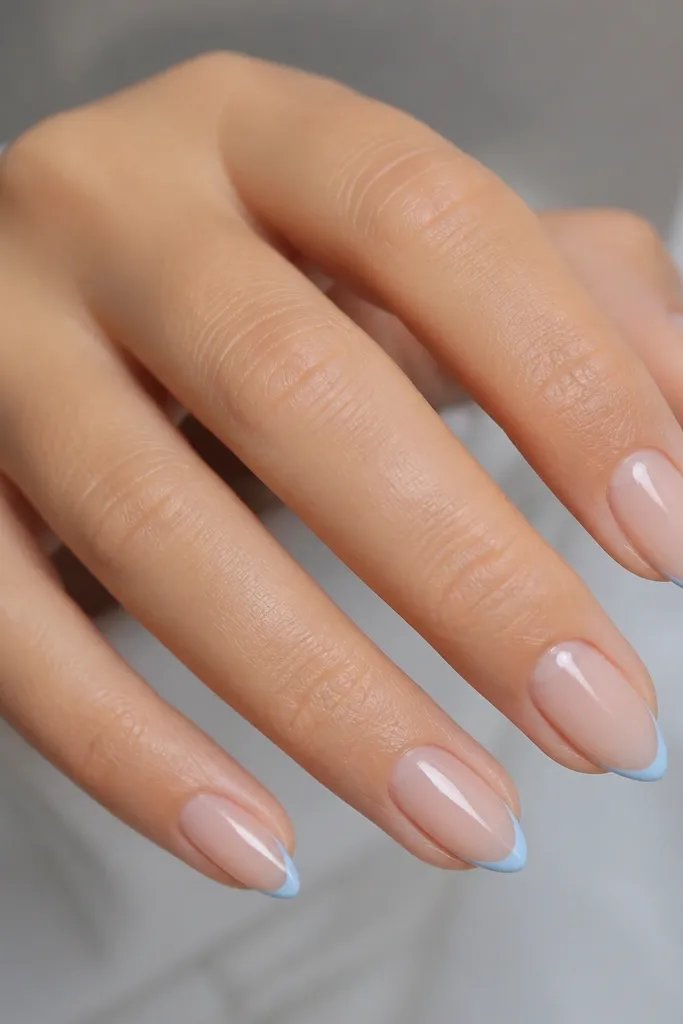 Short stiletto nails with sheer nude base and sky blue micro French tips, glossy top coat, clean cuticles.