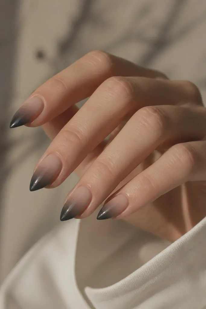 Short stiletto nails with a sheer nude base fading into charcoal gray at the tips, smoky gradient, glossy finish.