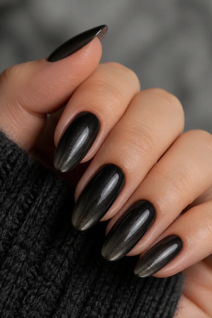 A black ombre fades from cuticle into a softer charcoal toward the tips, with graphite chrome concentrated along the tip area in a smooth fade.
