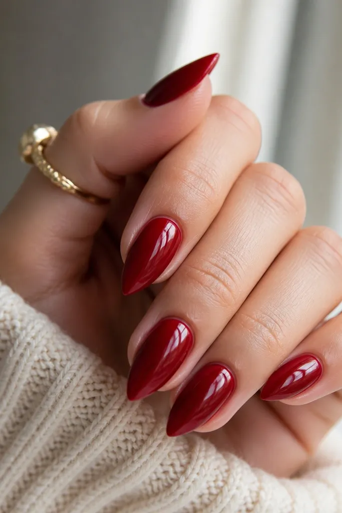 Five short stiletto nails in a deep cherry red with a mirror-like shine; the nails taper to a crisp point and the surface looks smooth like glass.