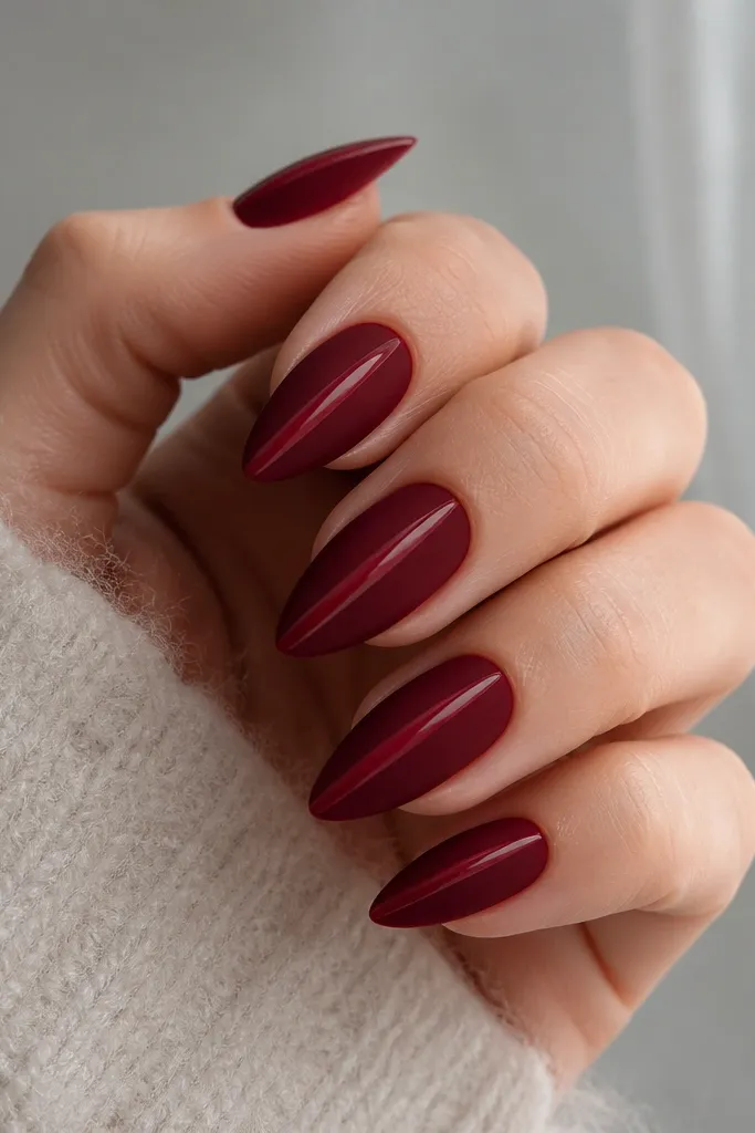 Short stiletto nails in deep red velvet matte; one thin glossy stripe runs down the center on each nail like a highlight line.