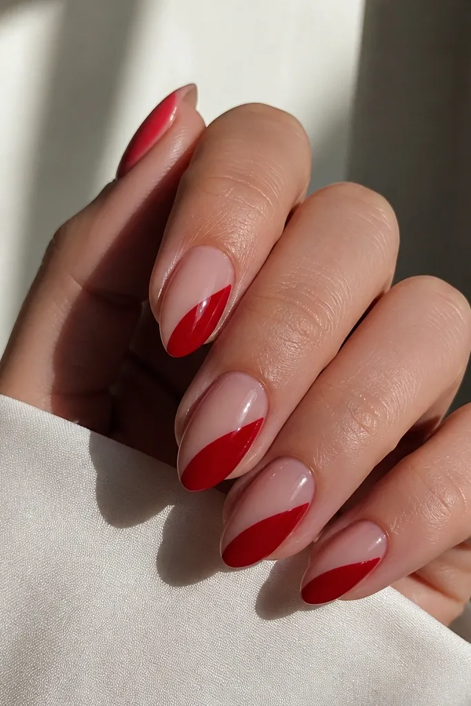Short stiletto nails with a sheer nude base; a glossy red diagonal panel runs from the lower left near the cuticle to the upper right near the tip.