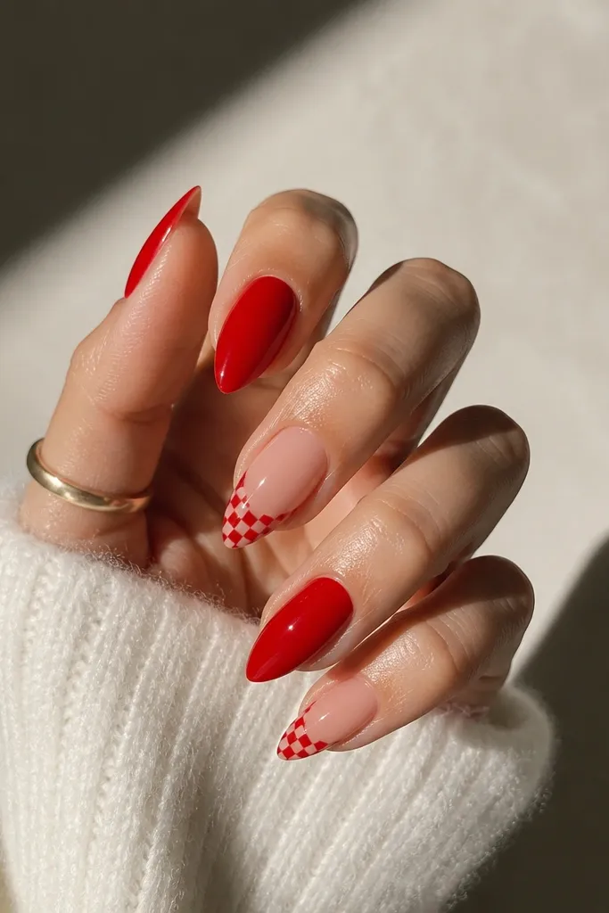 Short stiletto nails mostly in glossy red; two accent nails have a tiny red-and-nude checker pattern near the tip.
