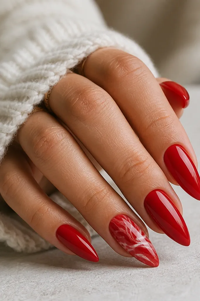 Short stiletto nails mostly solid glossy red; one accent nail has red marble swirls with thin white veining, all glossy.