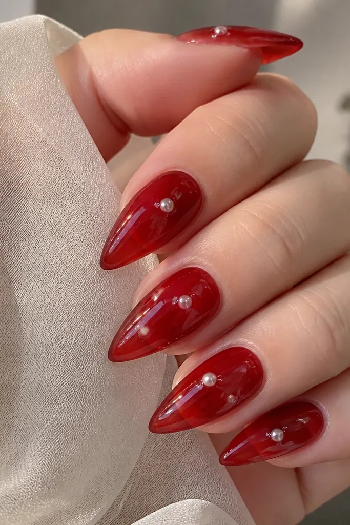 Short stiletto nails with deep red jelly translucence; small white pearl dots look like they are floating under the gel; glossy finish.
