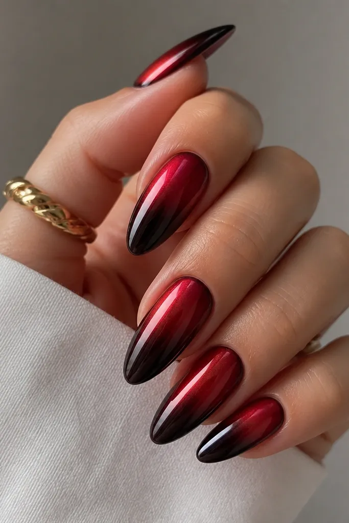Almond nails with a black-cherry ombre that starts near the cuticle as deep red and fades into near-black at the tips. Ruby red chrome sits on the top third, creating a glossy red mirror sheen.