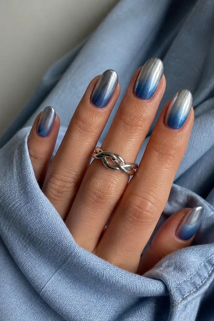 Short almond nails with a denim blue ombre fading from light blue at cuticle to deep blue at tips. Mirror steel chrome sits on the top third and looks like a cool silver sheen.