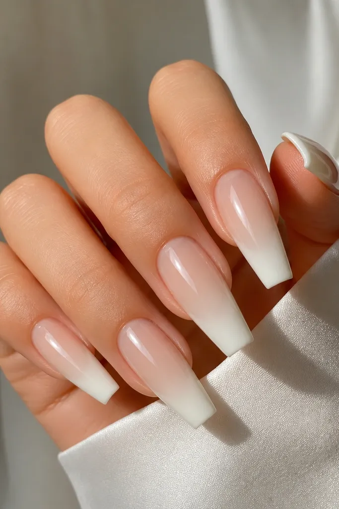 Acrylic coffin nails with warm beige sheer base; milky white French tips that look soft and creamy; glossy top coat; no gems.