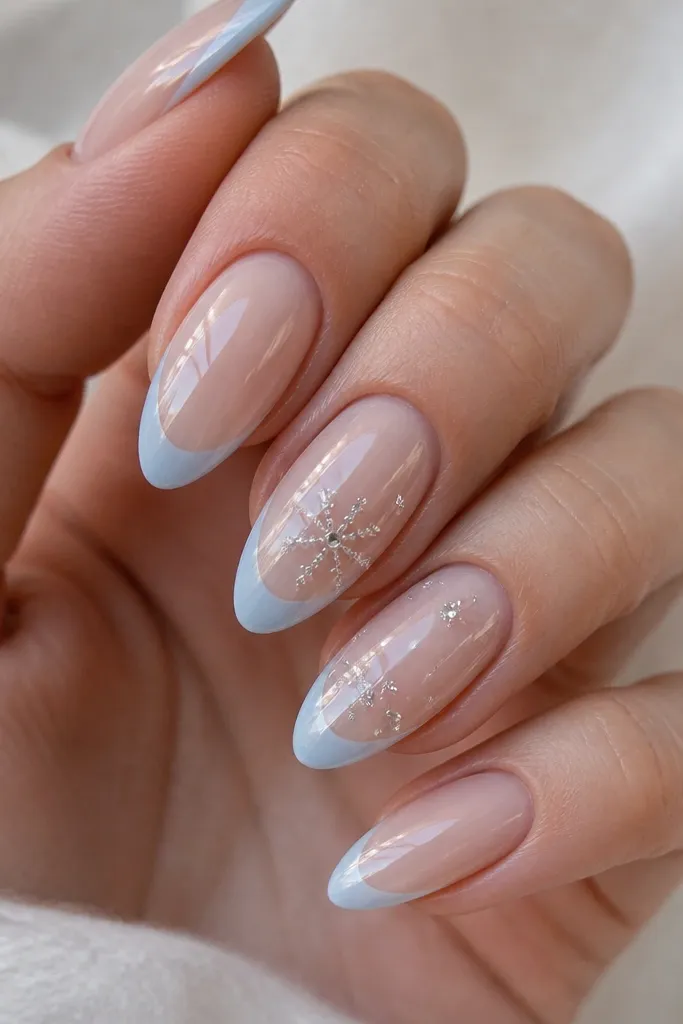Coffin nails with sheer nude base; icy blue French tips; tiny clear 3D dots arranged like snowflakes near the center of each tip; glossy top coat.