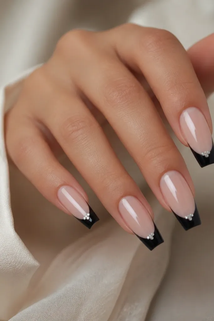 Coffin nails with sheer nude base; black French tips; small white stud cluster at the center of each tip; glossy finish.