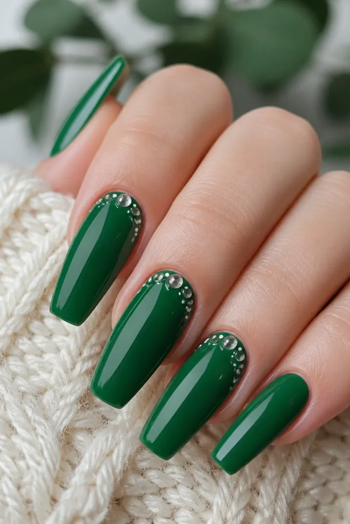 Short acrylic coffin nails painted glossy emerald green; two nails feature tiny clear-domed dots and micro white dots arranged near the cuticle.