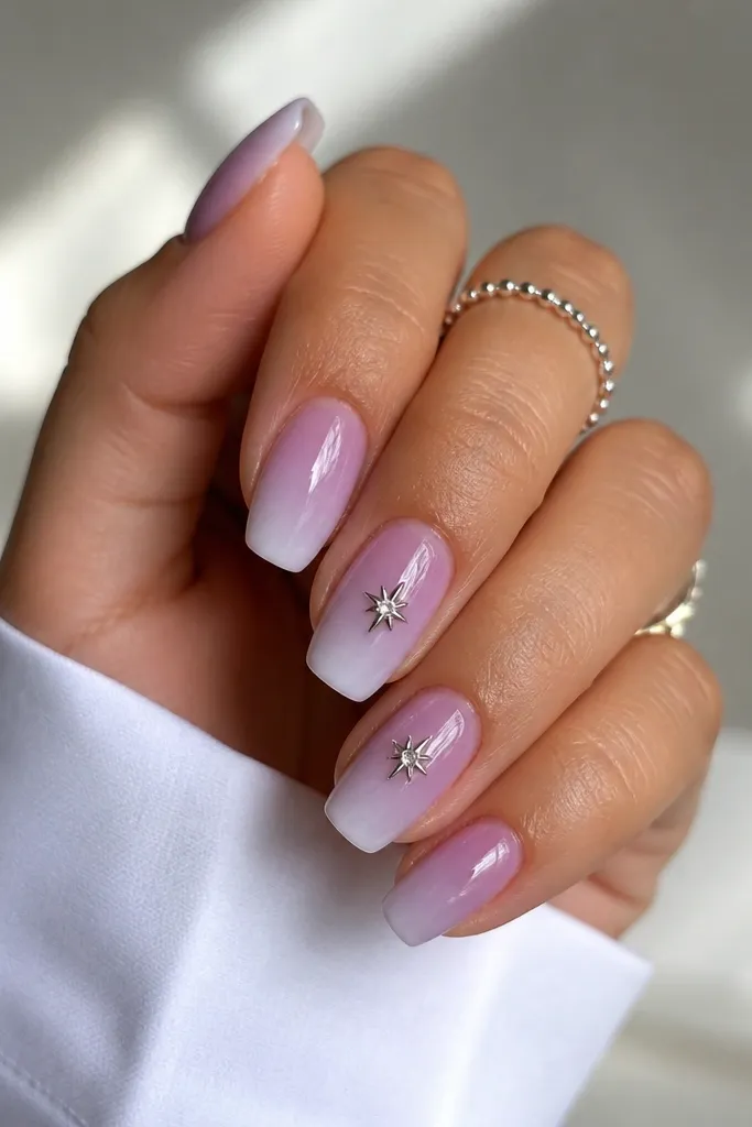Short acrylic coffin nails with a lavender mist gradient; tiny silver star charms sit on two nails, glossy topcoat over everything.