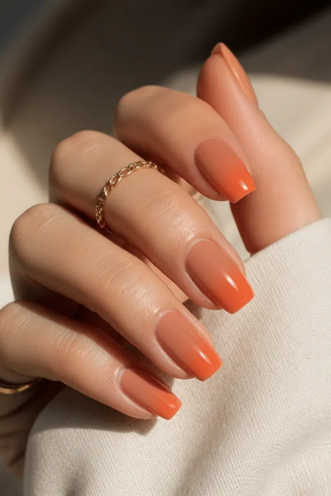 Short coffin nails with a terracotta nude base and soft orange tint at the tips, blended like a gradient; glossy topcoat.