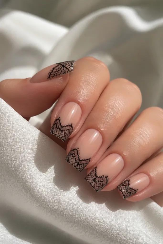 Short nude acrylic coffin nails with a black lace pattern overlay on the tips; the lace lines look like fine mesh; glossy topcoat.