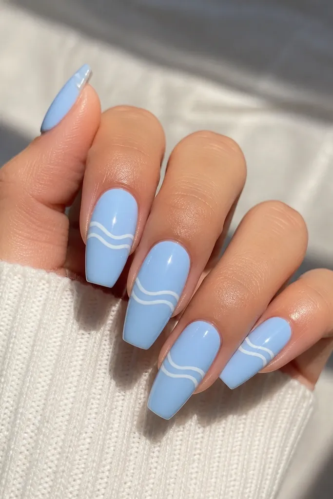 Short coffin nails painted baby blue. Each nail has one or two thin white wave lines running horizontally across the middle, glossy and clean.
