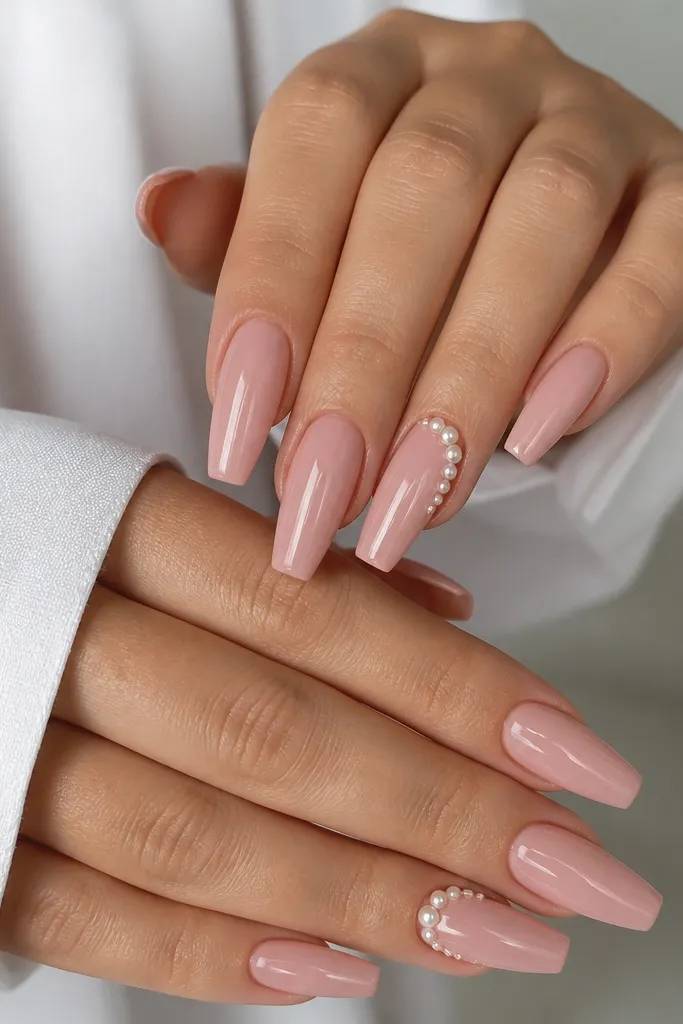 Glossy blush coffin nails with tiny pearl studs clustered in a line along the side of two accent nails.