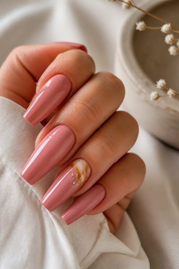 Warm pink glossy coffin nails with one accent nail showing a caramel swirl near the cuticle and a tiny dot cluster.