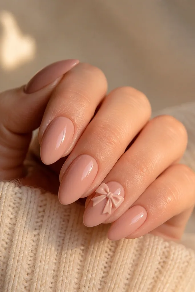 Glossy rose blush coffin nails with a small nude 3D bow charm on one accent nail; bow has a soft sheen.