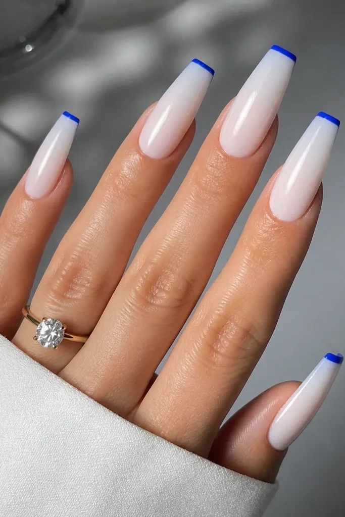 Long coffin nails with a milky sheer base, ultra-thin cobalt blue French tips, and a mirror-gloss finish. The cobalt line is straight and narrow, centered at the very edge.