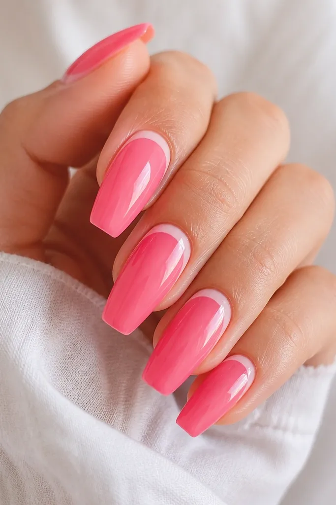 Coffin nails painted watermelon pink with a juicy glossy topcoat. Near the cuticle there's a thin white arc that curves around the nail, like a crescent highlight.