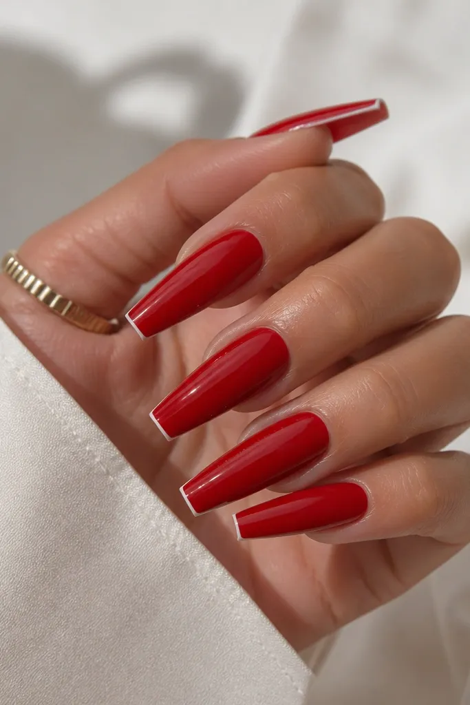 A hand with long red acrylic coffin nails; each nail has a very thin white line at the tip, almost like a hairline French, with a glossy finish.